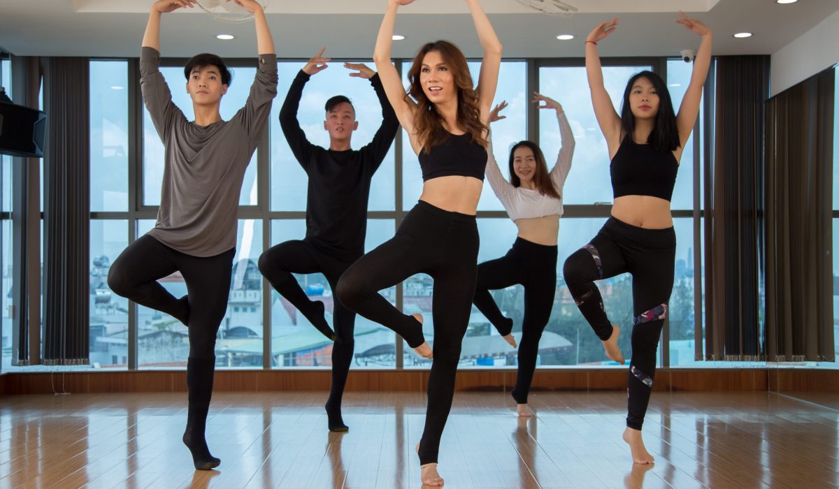 Group of slim Asian people standing on one foot and looking away while dancing in stylish studio